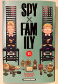 Couverture de Spy x Family Tome 11, deux garçons assis sur des chaises, objets variés au sol.