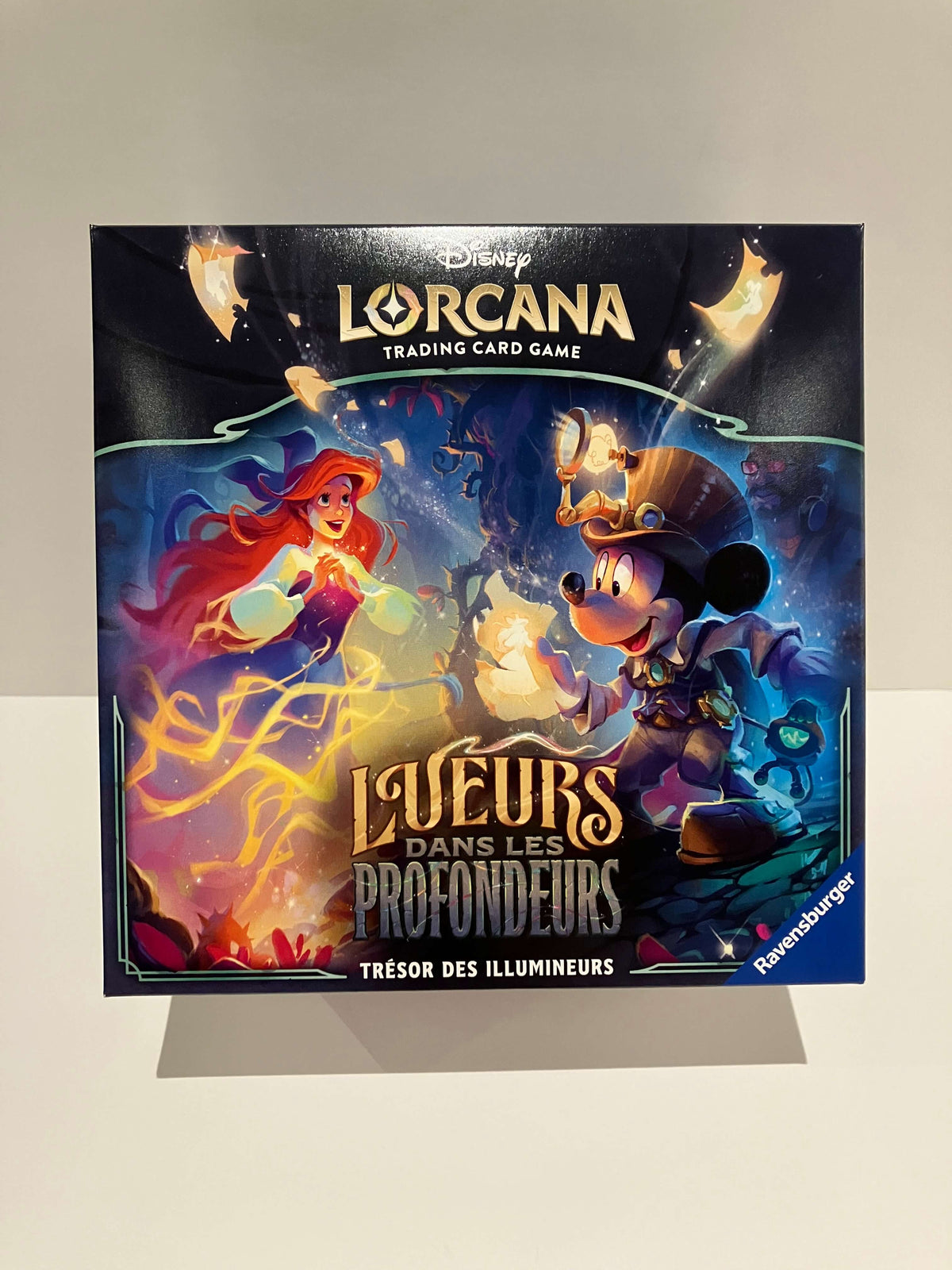 Trove pack Disney Lorcana Trading Card Game Lueurs dans les Profondeurs, illustrée avec Mickey et Ariel dans une forêt, contenant 8 boosters, 6 séparateurs de cartes illustrés, 1 boite de rangement, 1 compteur de Lore, 6 dés compteurs de dommages