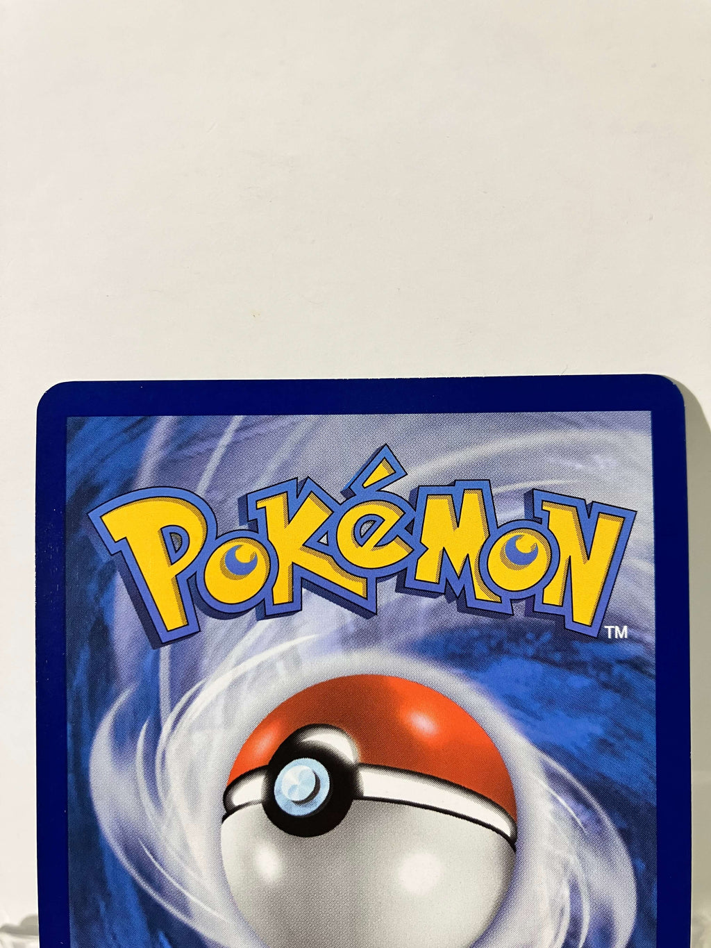 Dos d'une carte Pokémon avec logo jaune et Pokéball sur fond tourbillonnant bleu
