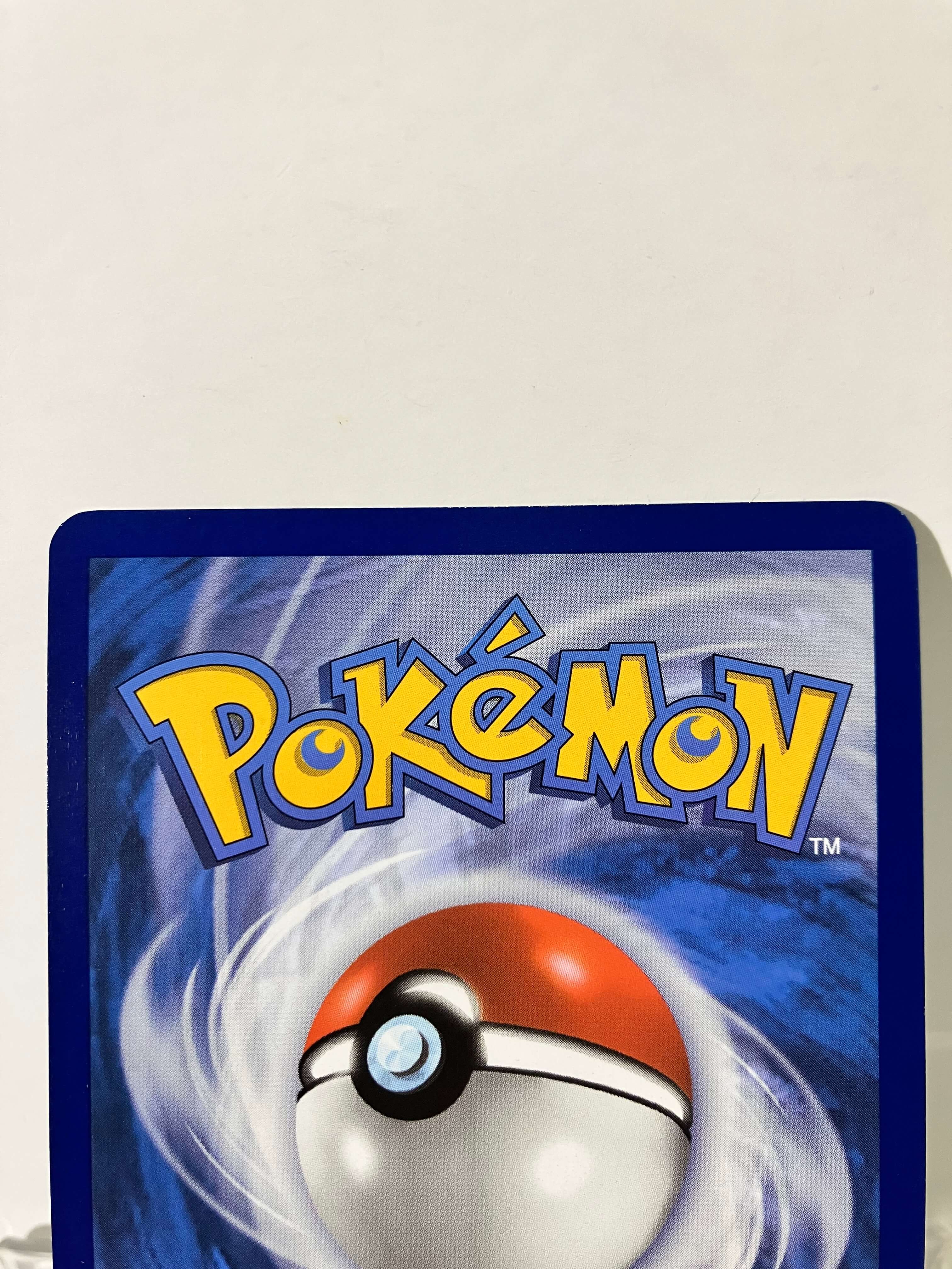 Dos d'une carte Pokémon avec logo jaune et Pokéball sur fond tourbillonnant bleu