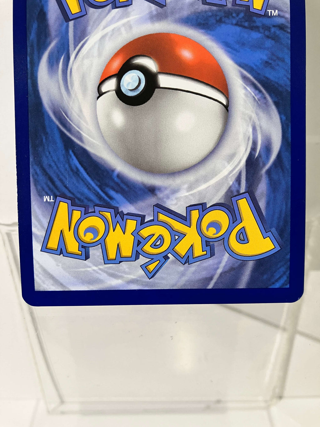 Dos d’une carte Pokémon, Pokéball au centre, carte dans une pochette plastique transparente.